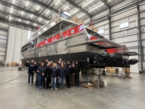 The Emerald Clipper crew wave next to the new vessel, under construction at Mavrik Marine, Inc